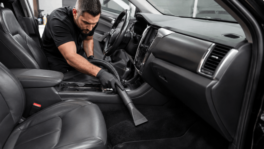 Automotive detailing services vacuuming the seats and carpets inside a vehicle.