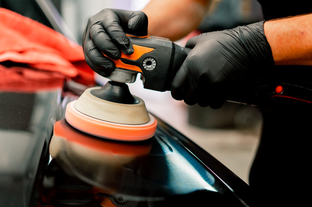 A person wearing black gloves is polishing a car's surface to enhance its shine and appearance.