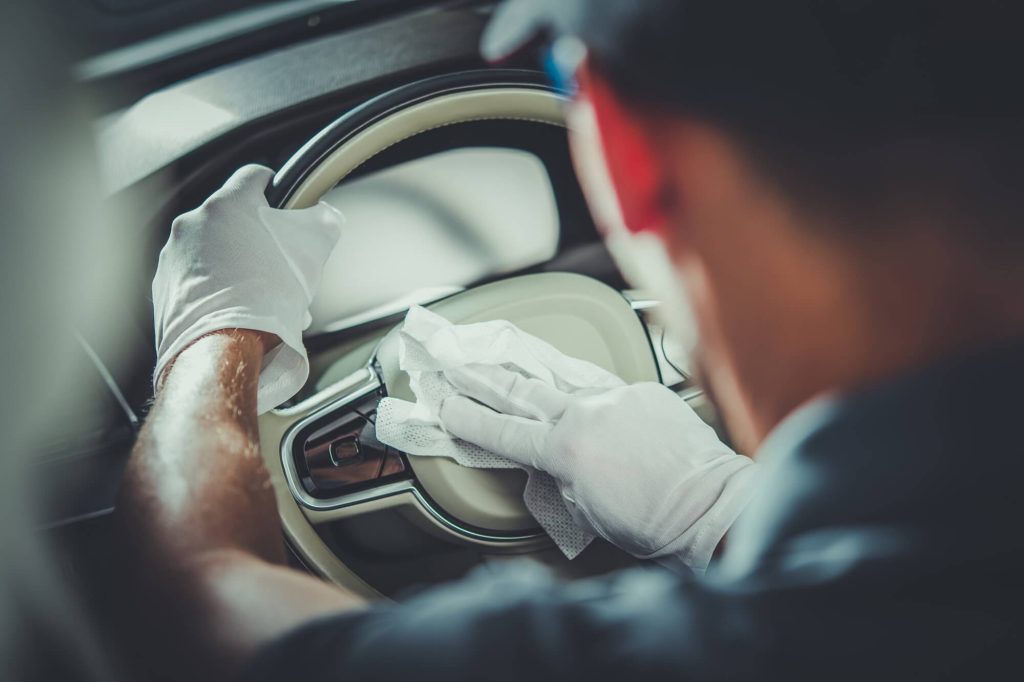 A man wearing white cleaning gloves cleans the wheel of a Mercedes Benz.